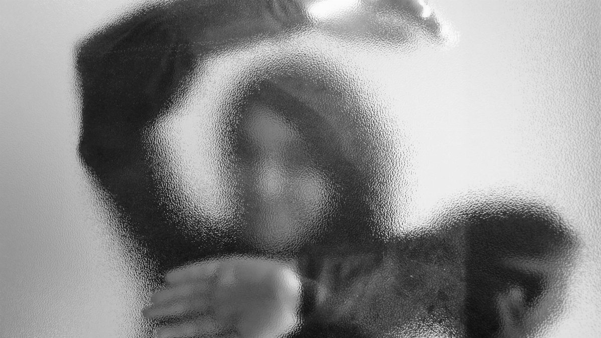 A mysterious silhouette of a person behind frosted glass creating an abstract artistic visual.