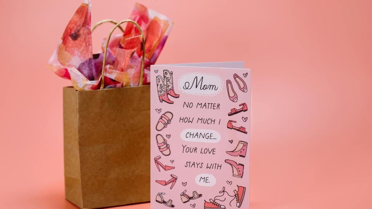 Mother's Day card with heartfelt message and gift bag on pink surface.