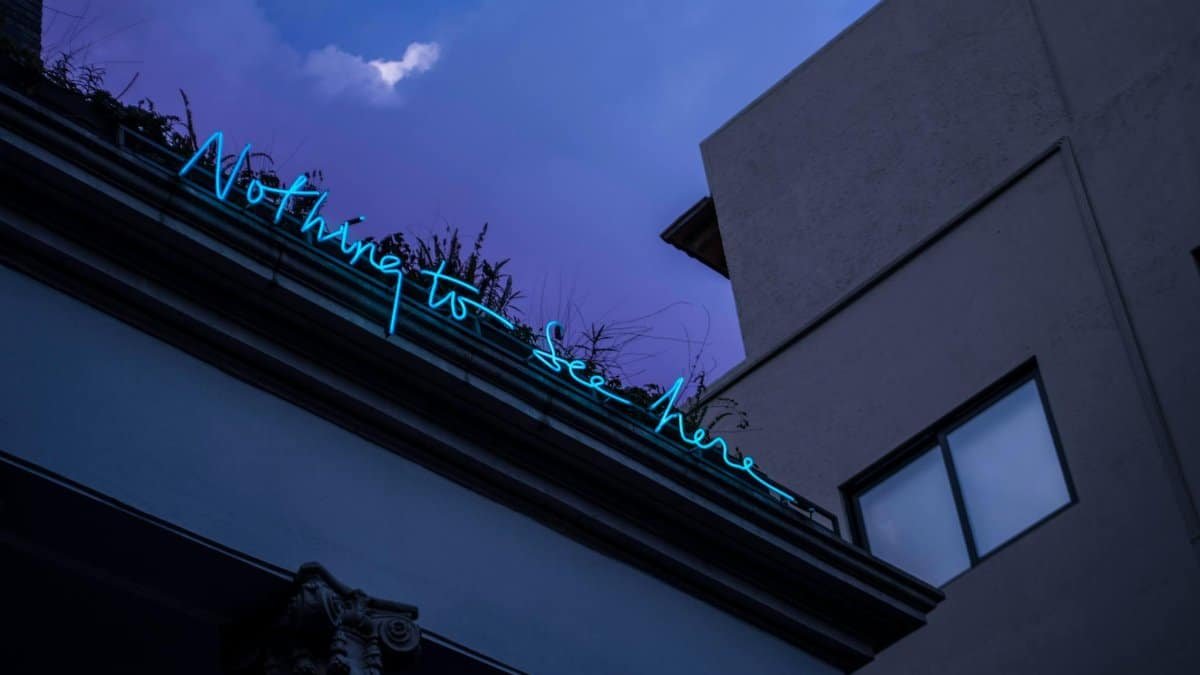 Low-angle shot of a neon sign reading 'Nothing to See Here' against a city night sky.