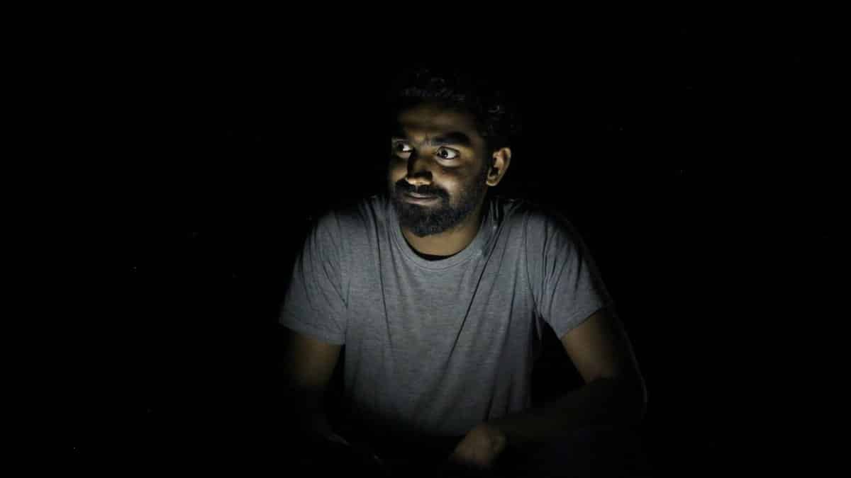A thoughtful man with facial hair illuminated by dramatic low light, creating a moody portrait.