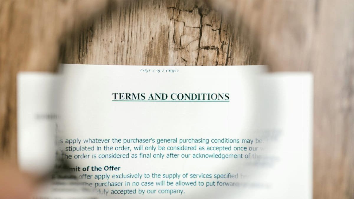 Magnifying glass focusing on terms and conditions document on wooden surface.