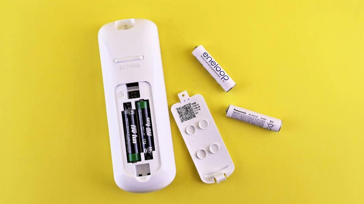 Close-up of remote control and batteries on vibrant yellow surface.