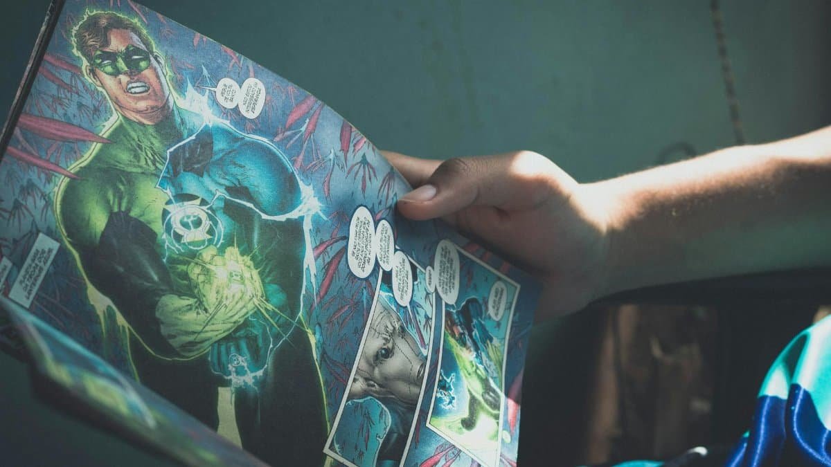 Close-up shot of hands holding a colorful superhero comic book in a sunlit room, depicting leisure reading.