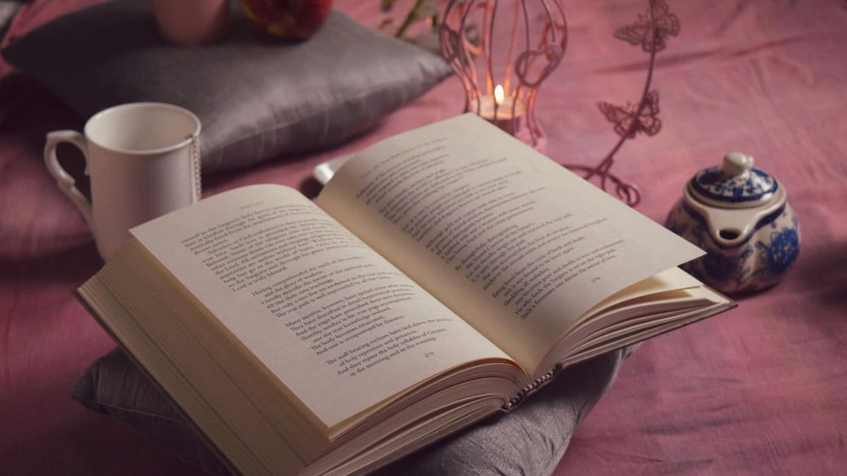 Inviting reading setup with an open book, tea, and candlelight on a cozy pillow arrangement.