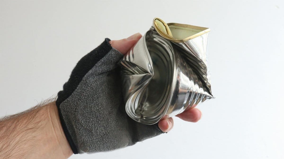 A gloved hand holding a crushed tin can showcases recycling and waste management.