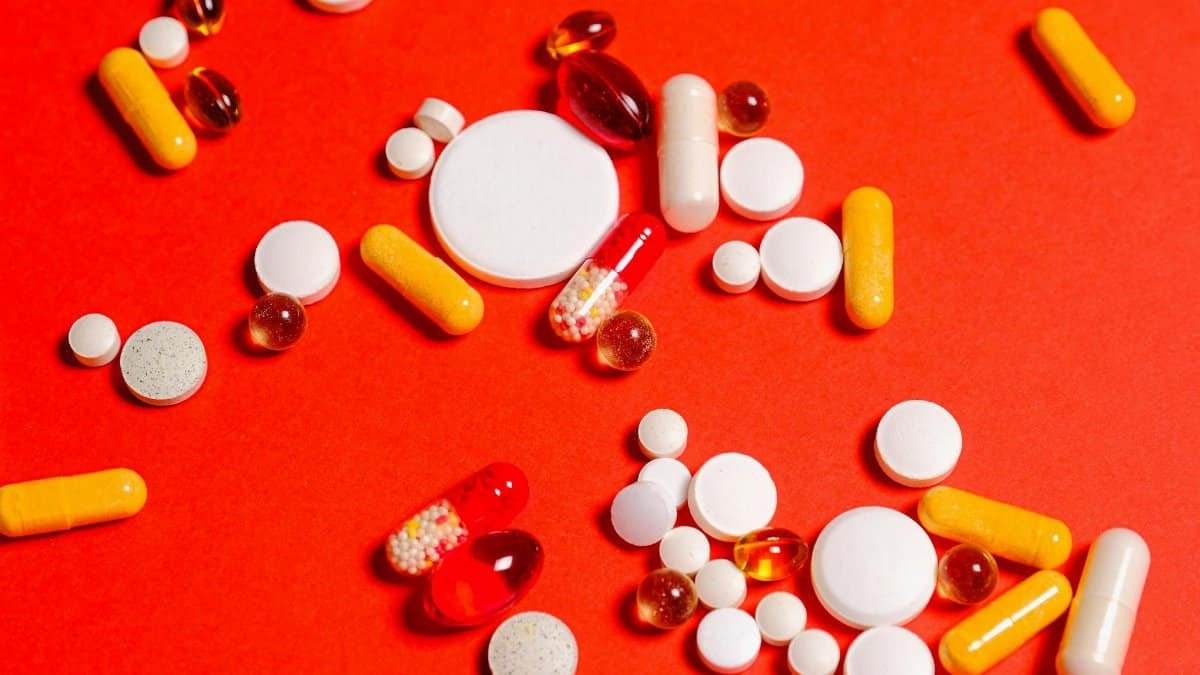 Variety of pills and capsules scattered on vibrant red backdrop, showcasing diverse medicine forms.