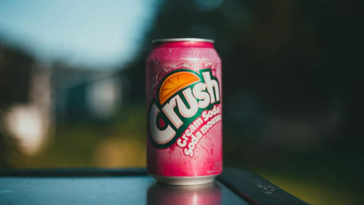 A vibrant pink Crush cream soda can placed on an outdoor table, captured in natural light.