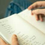 Close-up of a person taking notes in a notebook, writing a to-do list with a pencil.