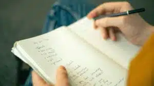 Close-up of a person taking notes in a notebook, writing a to-do list with a pencil.