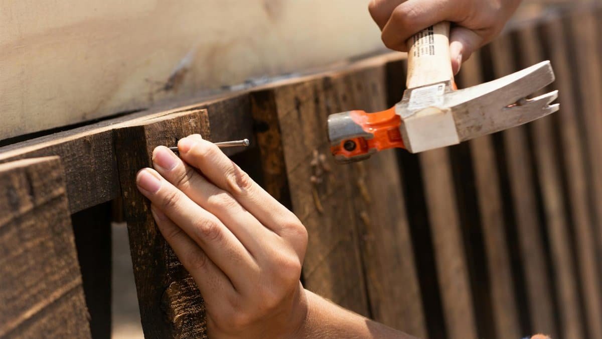 A detailed image showing hands hammering a nail into wooden planks, emphasizing carpentry work.