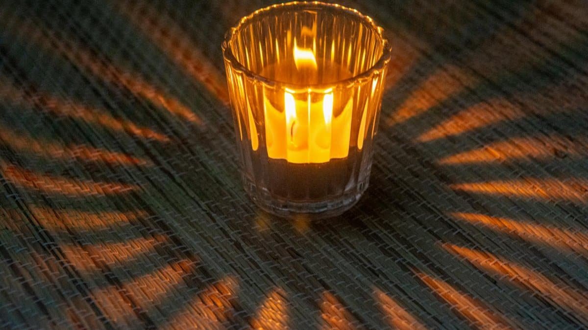 A single wax candle burns with radiant light, casting dramatic shadows.
