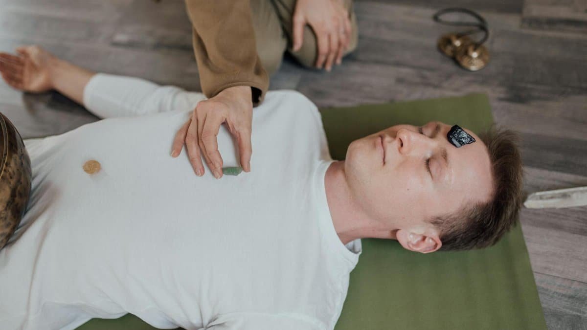 A man lies peacefully with crystals during a chakra healing meditation session indoors.
