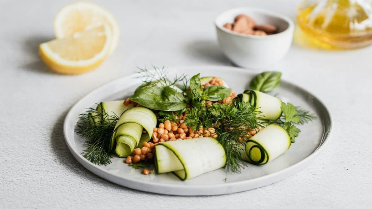 A beautifully plated fresh zucchini salad with lentils, herbs, and a lemon garnish.