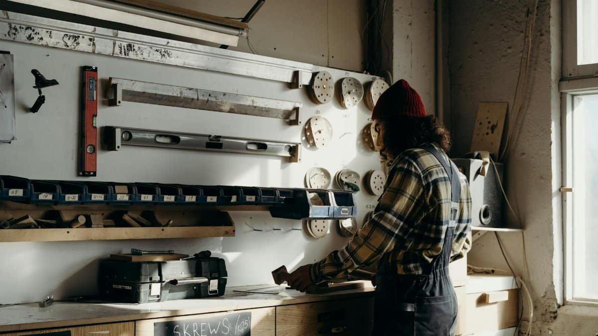 A craftsman focuses on carpentry tasks in a sunlit workshop, surrounded by tools.