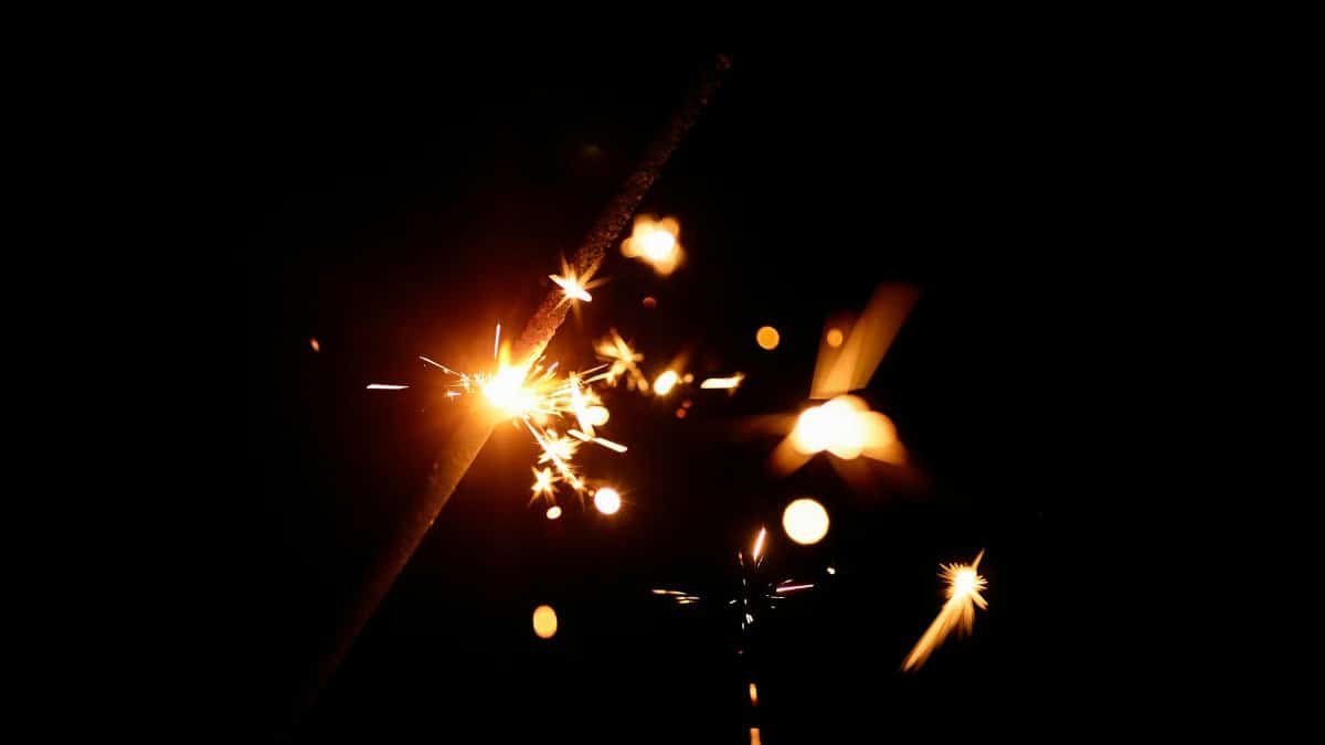 Close-up of a bright sparkler igniting against a dark background, creating magical sparks.