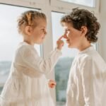 Two happy siblings enjoy a lighthearted moment indoors. Natural lighting enhances the playful mood.