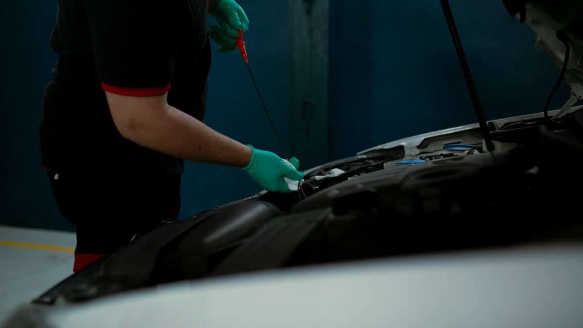 Mechanic in gloves checking engine oil level in a vehicle at an indoor workshop.