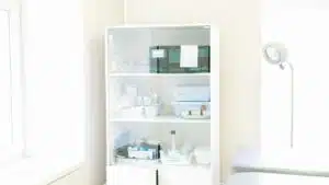 Modern white cabinet with cupboard with various medical instruments and shelves with medical materials near empty white bed near window and lamp in hospital