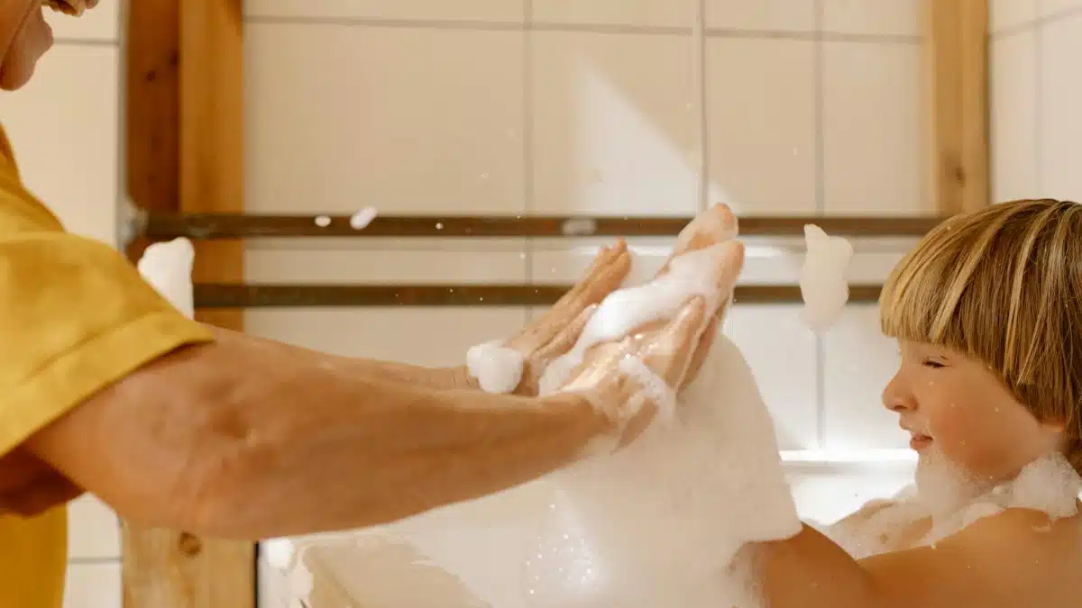 A joyful moment of a child playing with soap suds during bath time, showcasing family bonding indoors.