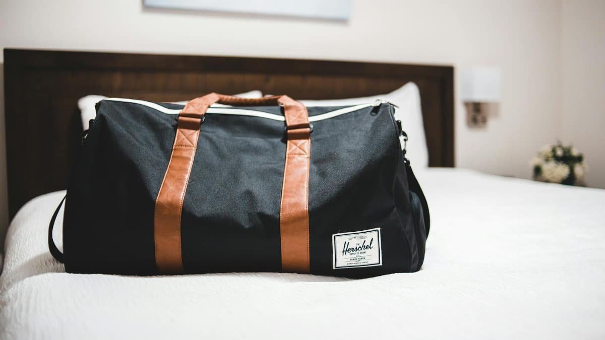Contemporary baggage bag with inscription on white bed cover in light hotel room