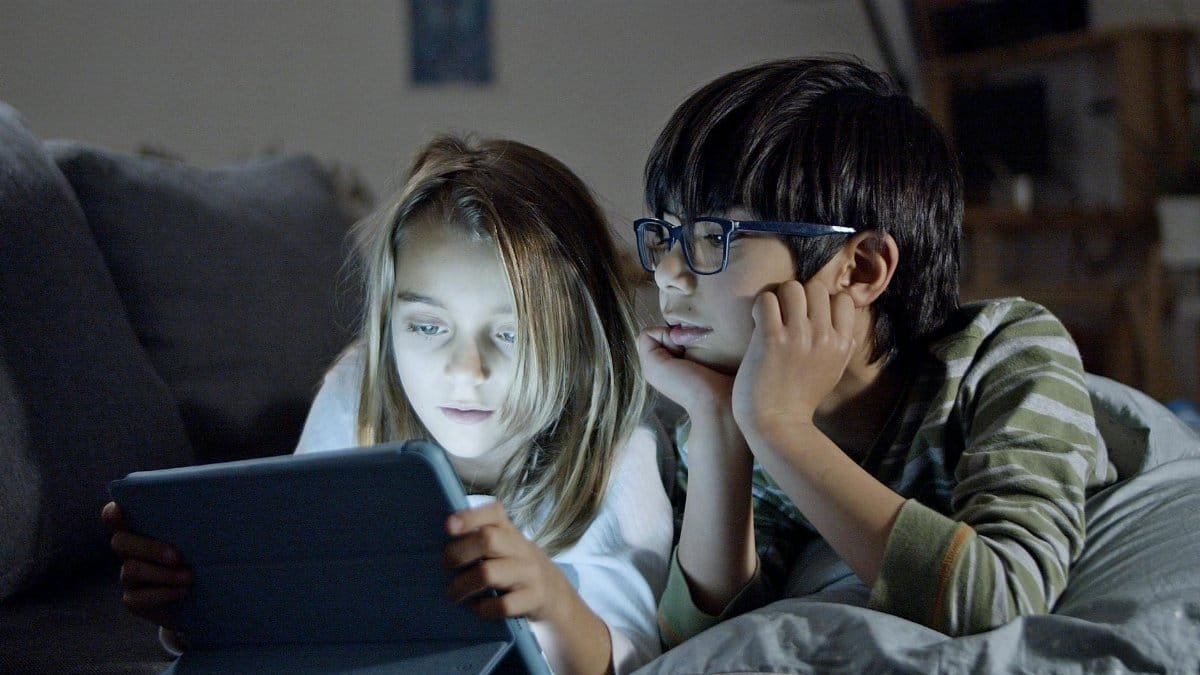 Two children using a tablet in a cozy home setting, engaging in screen time.