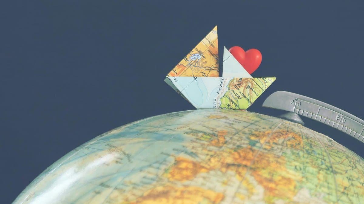A creative composition featuring an origami ship using a map, perched on a globe with a heart symbol, symbolizing global love and travel.