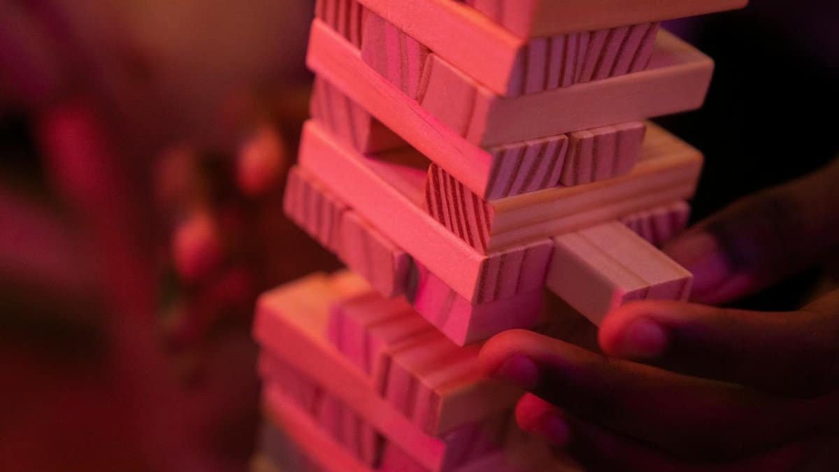 Close-up of hands playing a wooden block stacking game with pink lighting, capturing concentration and balance.