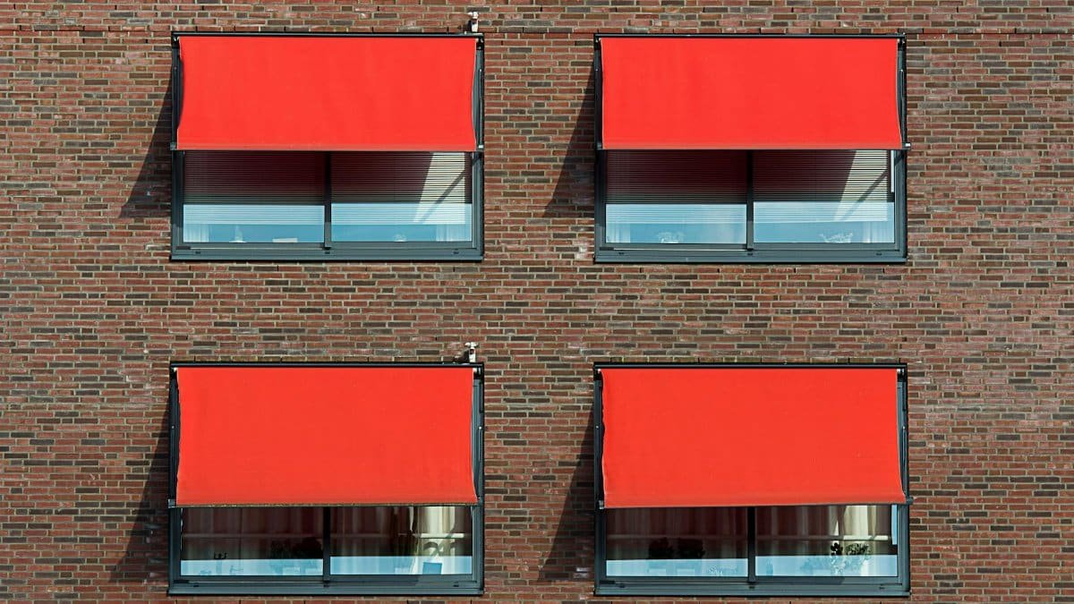 Symmetrical brick wall with four red sun shades covering windows.