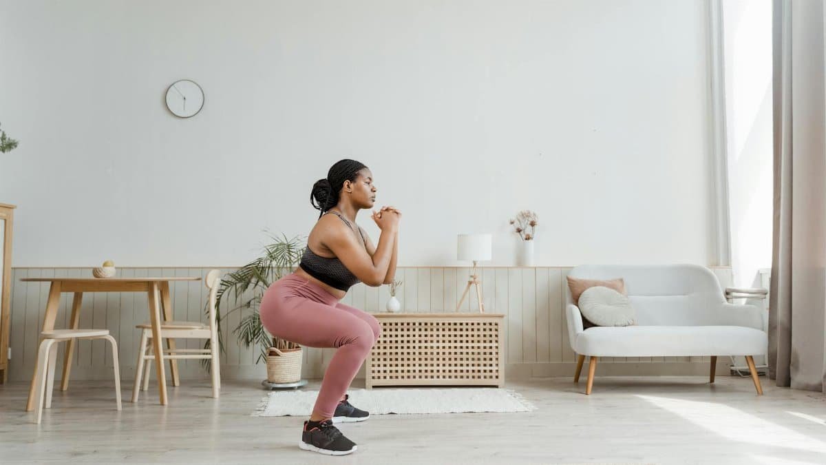 Woman in activewear doing squats at home, promoting a healthy lifestyle and fitness routine.