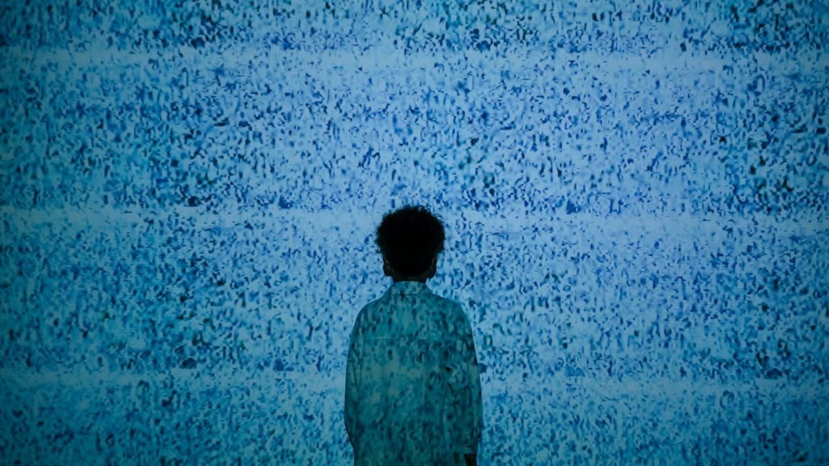A child stands silhouetted against a wall showing static noise, evoking themes of media influence.