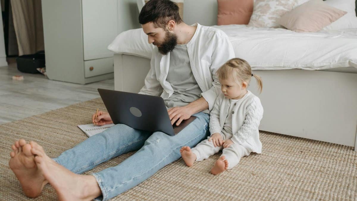 Father with laptop and daughter in bedroom demonstrating home lifestyle and remote work balance.
