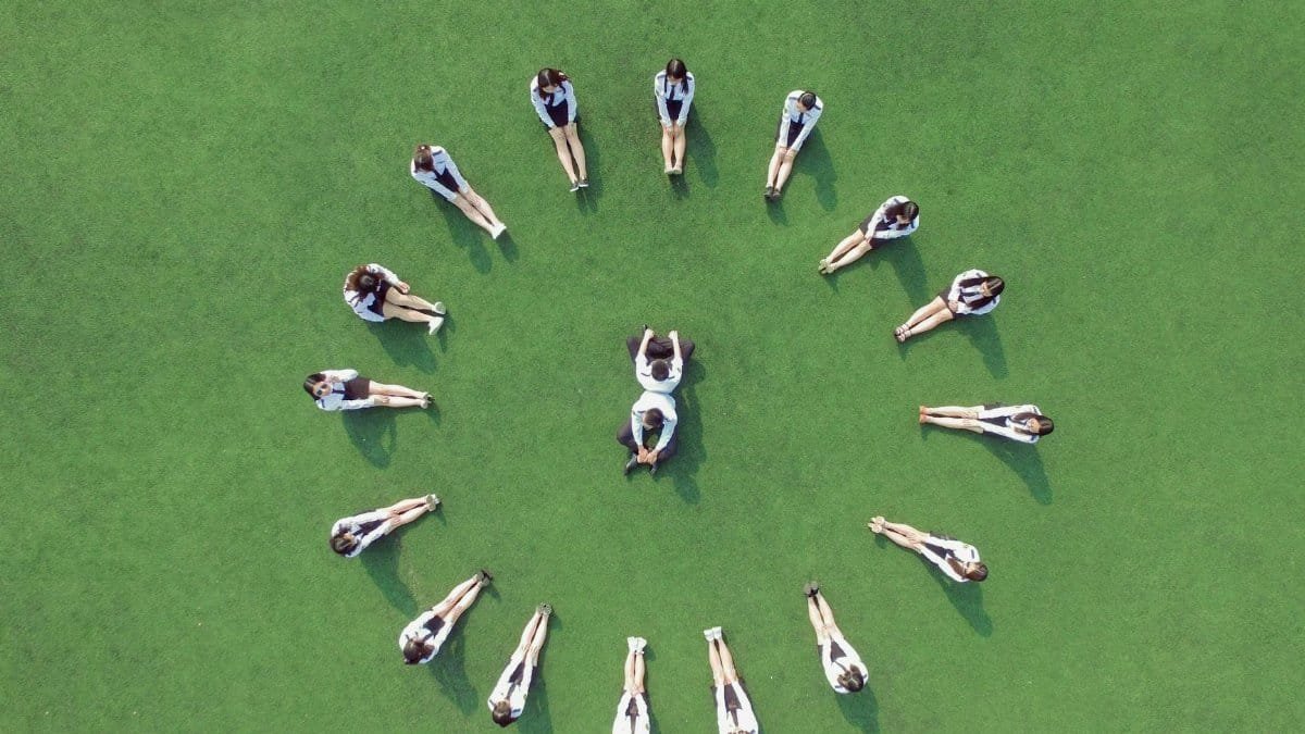 Group of students in uniform forming a circle on a green field, aerial shot.