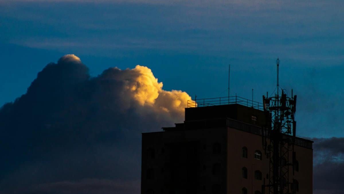Part of tall residential building with metal constructions located on street against blue sky with white cumulus clouds in city