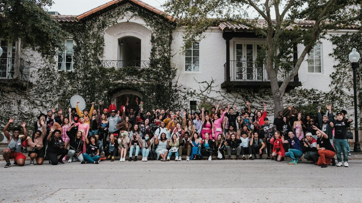 A diverse group poses enthusiastically in front of an ivy-covered building in Winter Park, Florida.