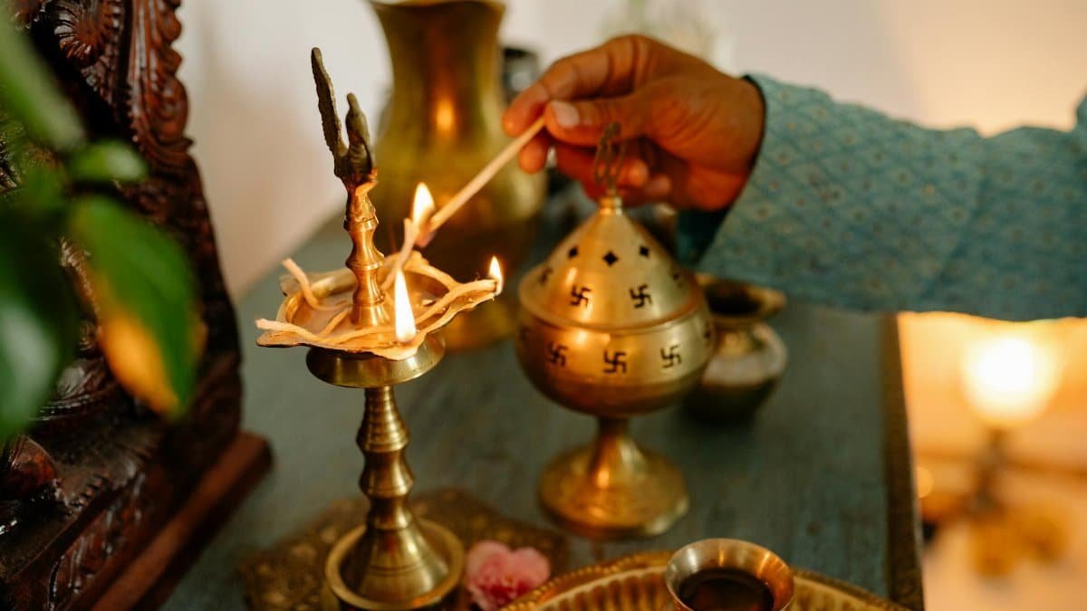 A hand performing a ritual with a brass lamp and incense burner, symbolizing spirituality.
