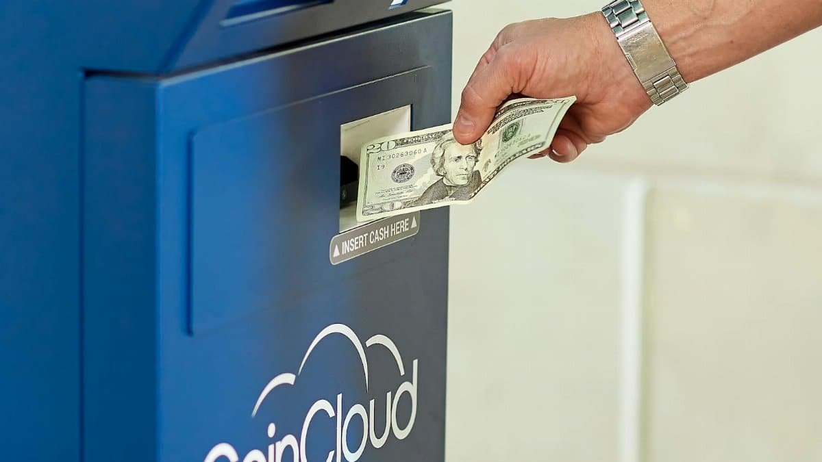 Hand inserting cash into a CoinCloud ATM, illustrating cryptocurrency exchange process.