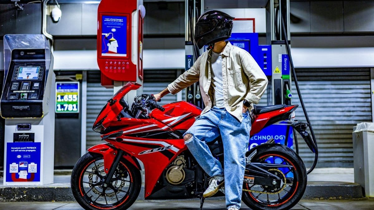 Motorcyclist refuels red sports bike at nighttime gas station.