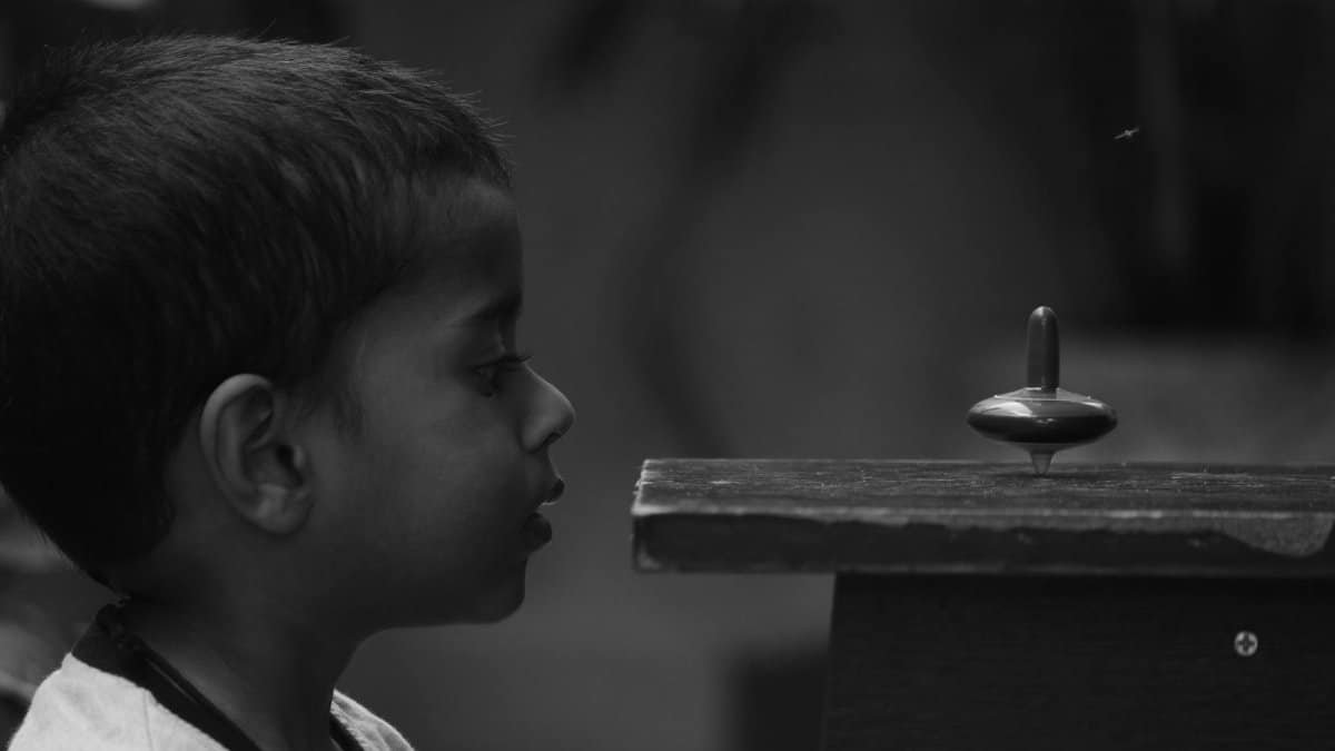 A mesmerized child gazes at a spinning top toy, capturing childhood wonder.