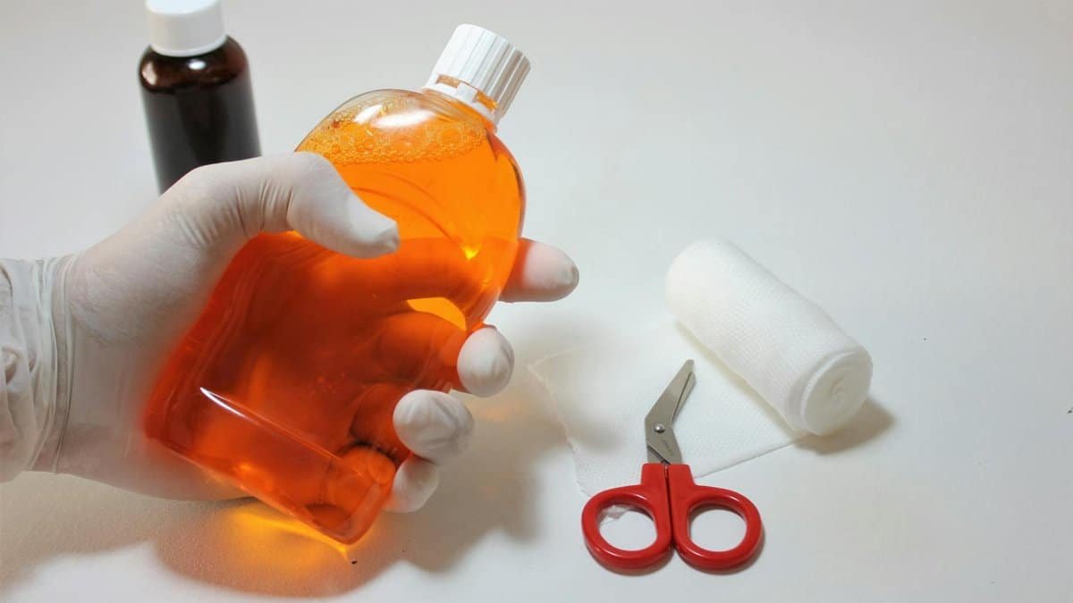 Hand holding orange antiseptic bottle with first aid items, ideal for healthcare themes.