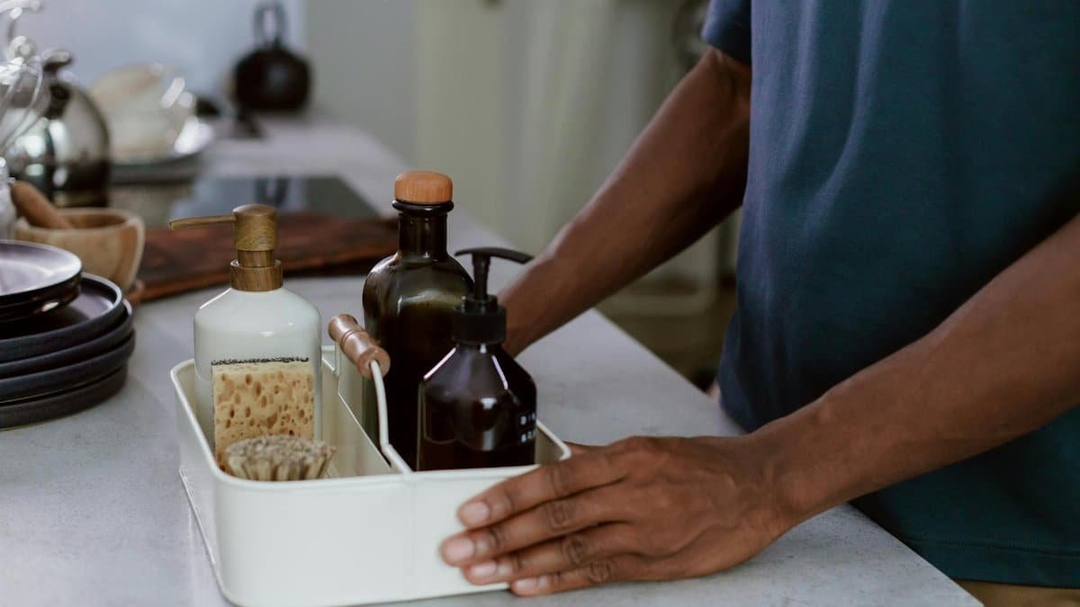 A close-up of a man organizing cleaning products in a modern kitchen environment.