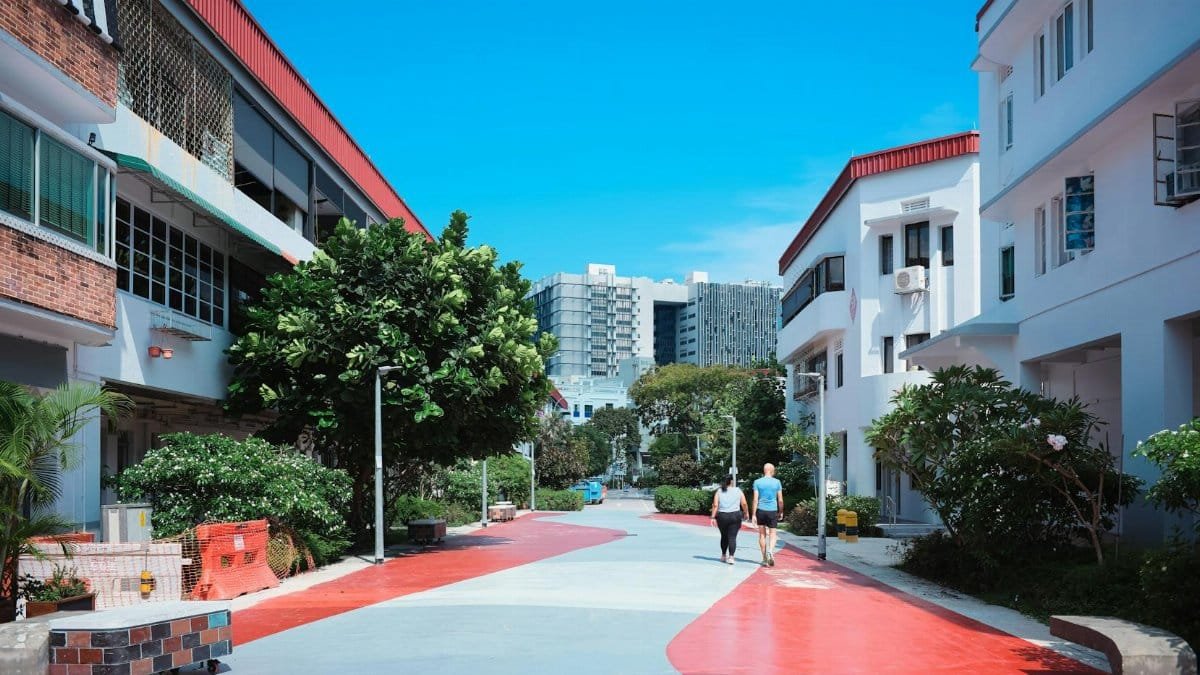 A colorful urban street scene with modern buildings and lush greenery under a clear blue sky.