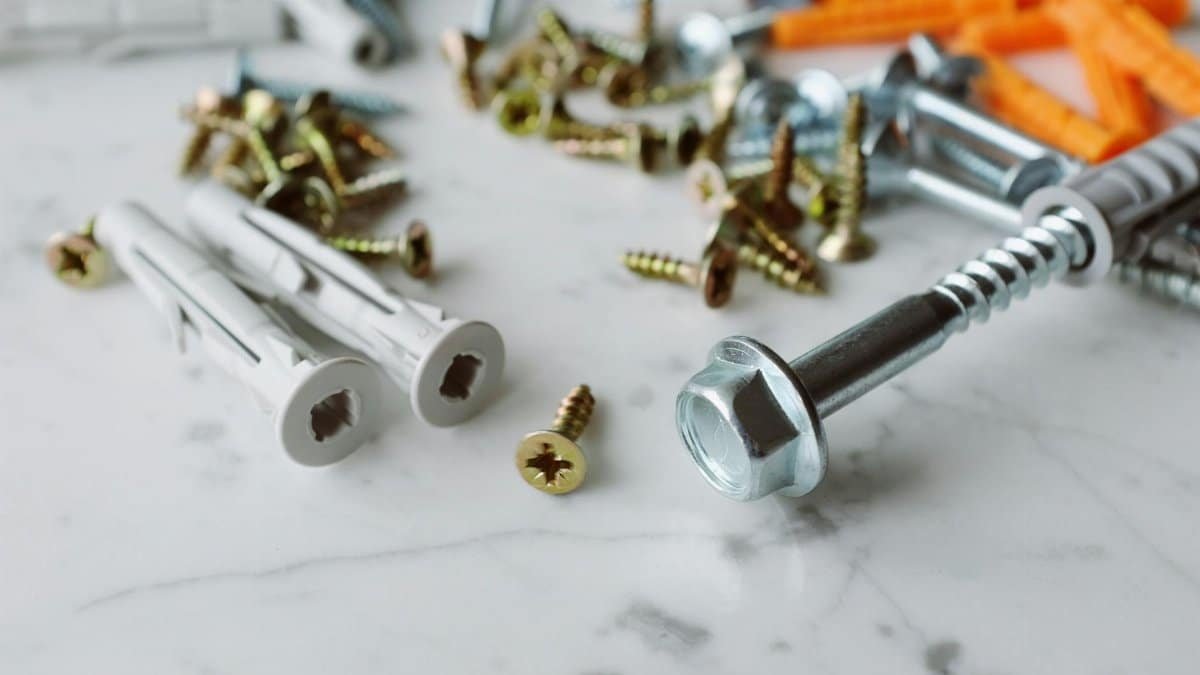 Closeup view of various multicolored plastic dowels with metal screws of different sizes placed on white marble table in modern workshop