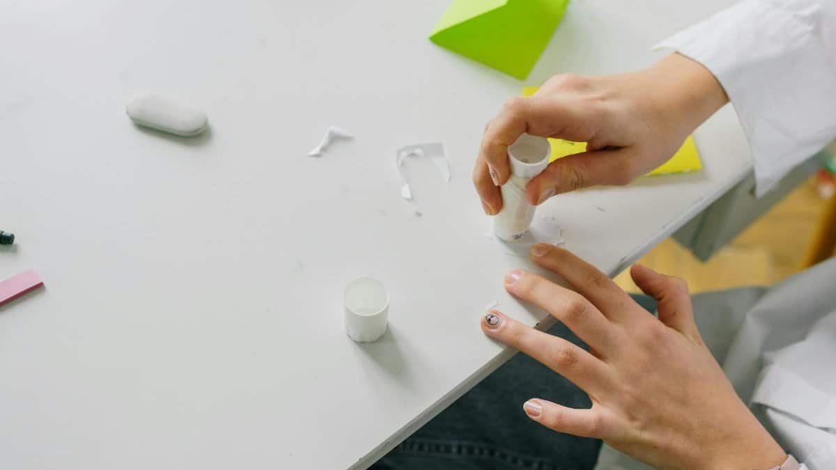 Close-up of hands applying glue stick on paper for a craft project on a desk.