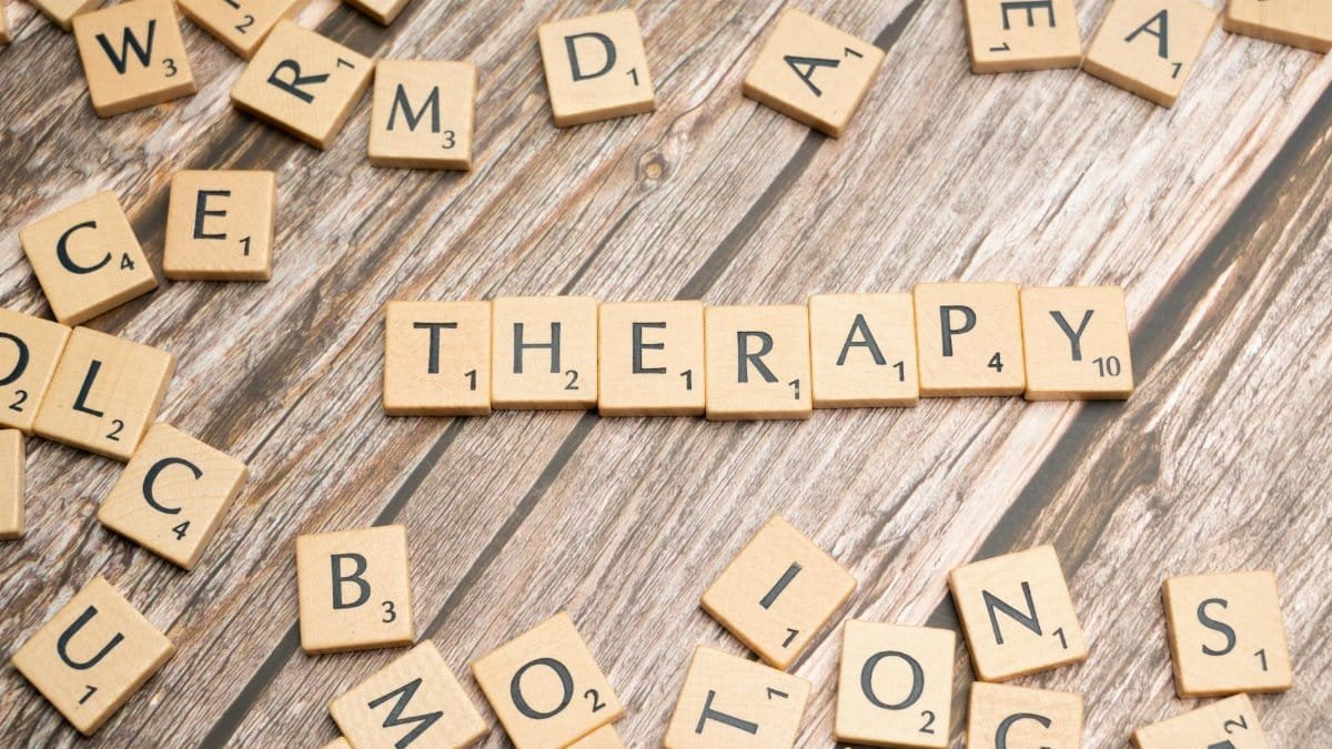Wooden letter tiles spelling 'therapy' on a wooden background, emphasizing mental health.