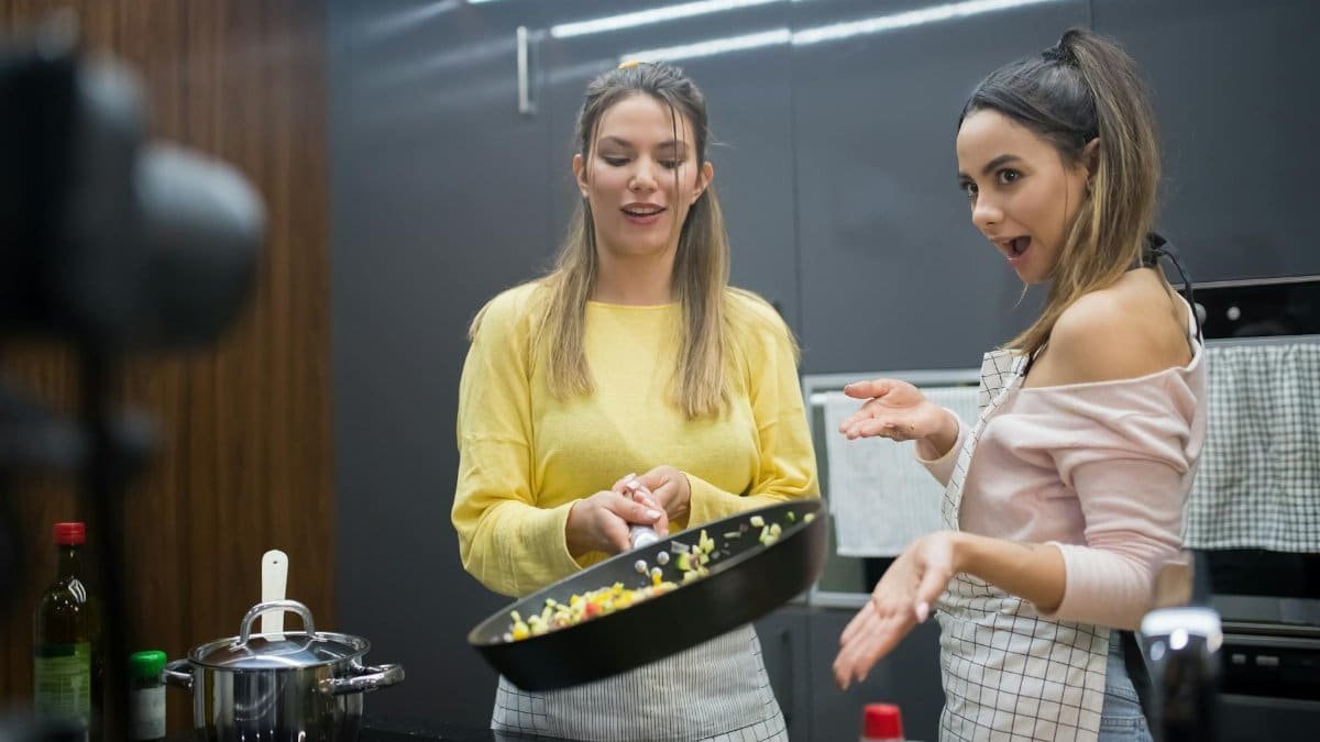Two young women cooking together in a stylish kitchen, engaging in a fun culinary activity.