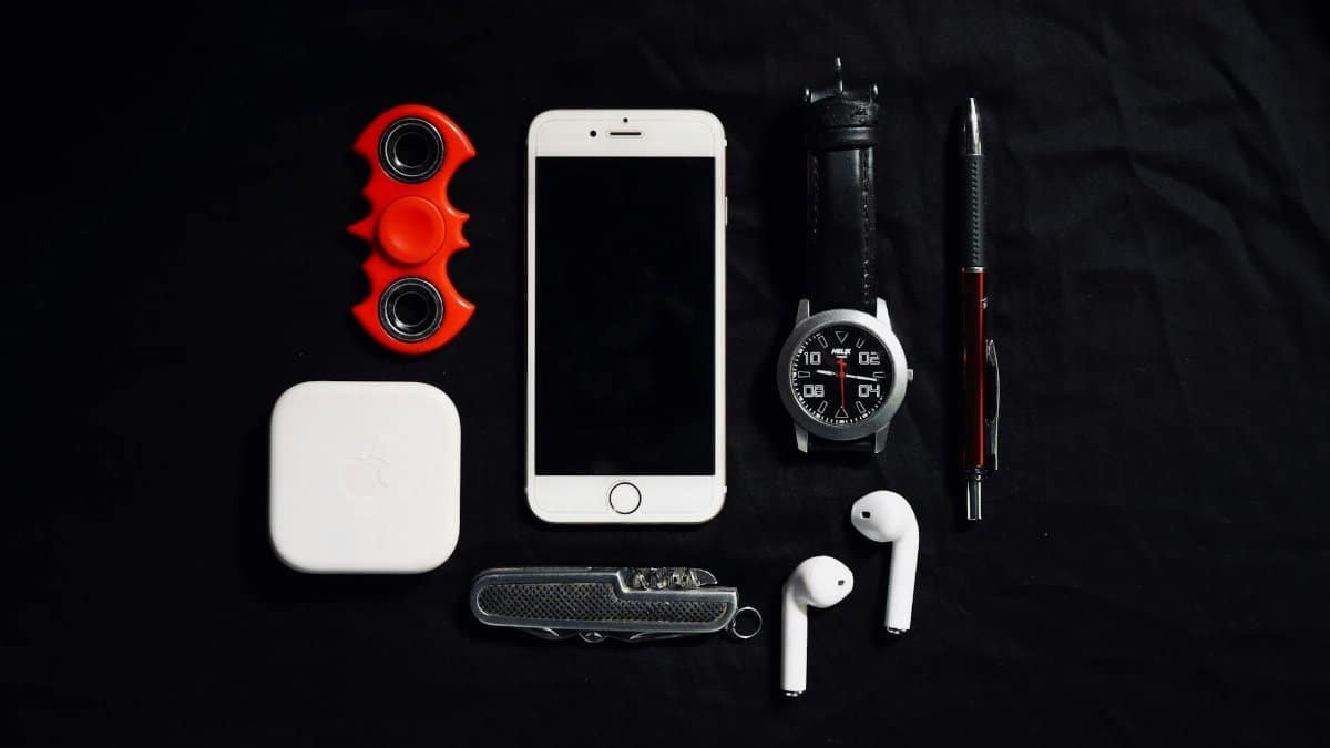 Flat lay photograph of essential everyday carry items including a smartphone, smartwatch, and fidget spinner.