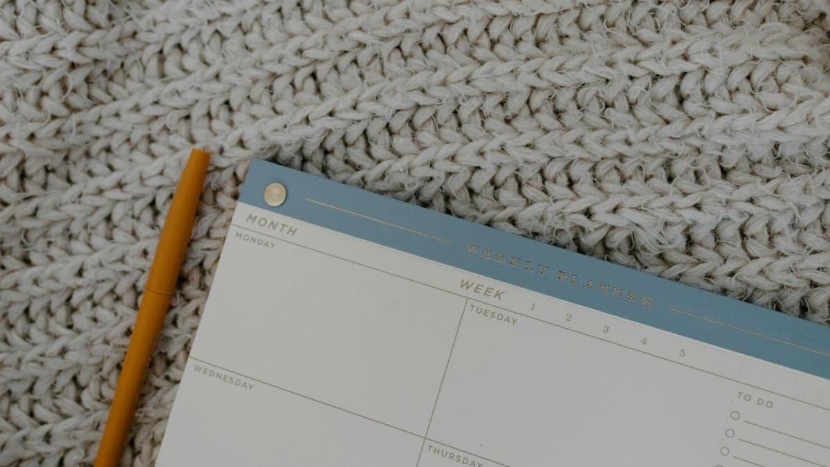 Weekly planner and pen on knitted fabric, perfect for organizing plans.