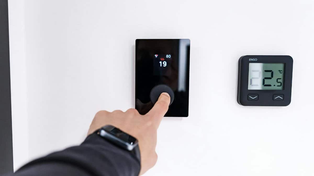A hand adjusting a digital thermostat in a modern home interior, showcasing smart home technology.