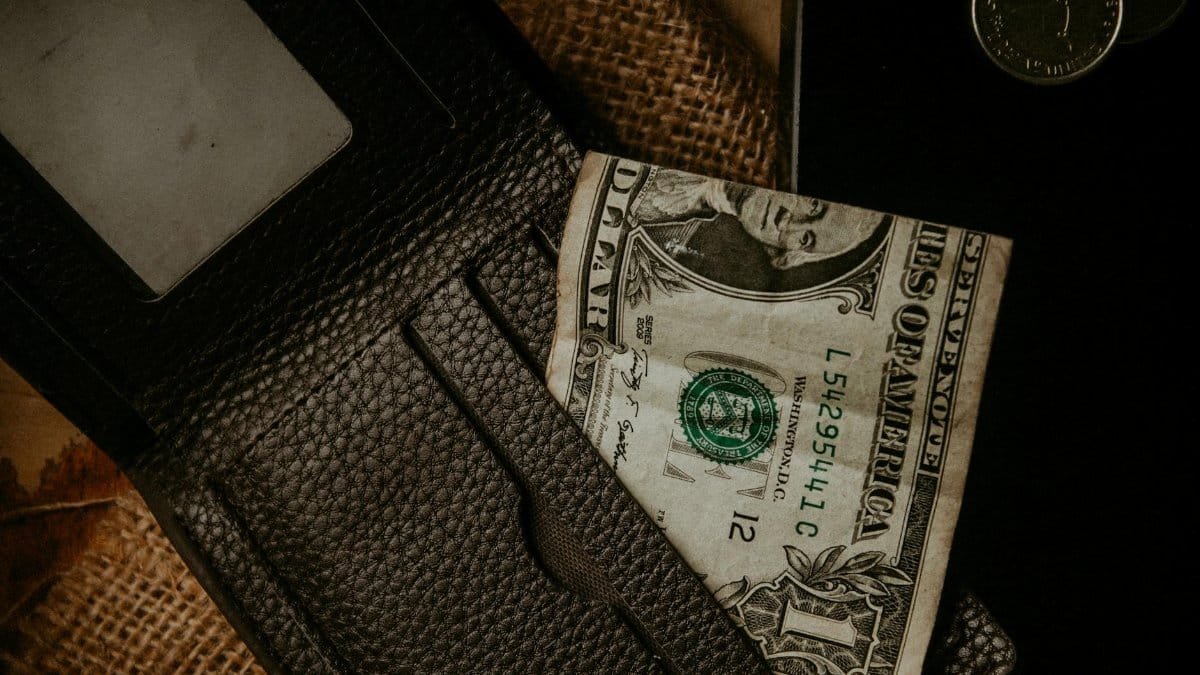A close-up view of a leather wallet with a one dollar bill and coins, highlighting personal finance concepts.