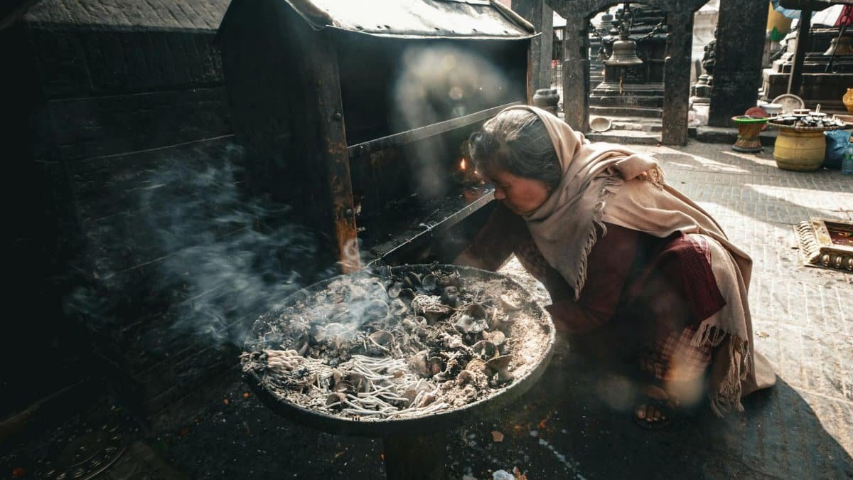 A woman in traditional attire tends a fire on a bustling street, adding warmth and cultural depth.